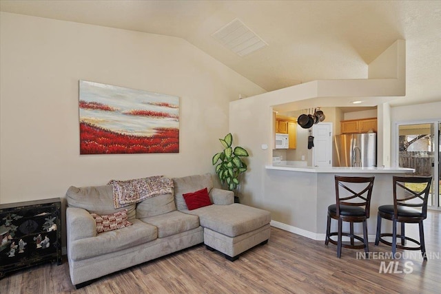 living room featuring vaulted ceiling, wood finished floors, visible vents, and baseboards