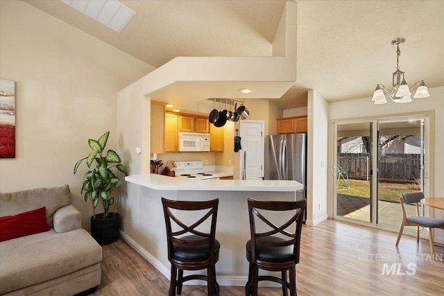 kitchen with a breakfast bar area, light countertops, white microwave, freestanding refrigerator, and range