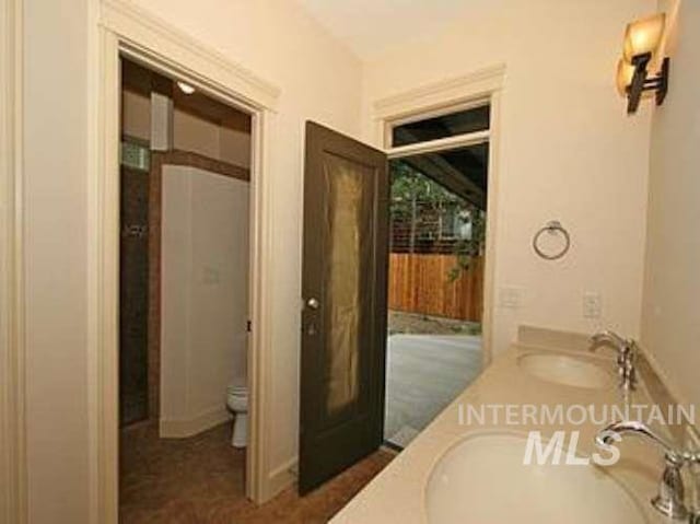 bathroom with toilet and dual bowl vanity