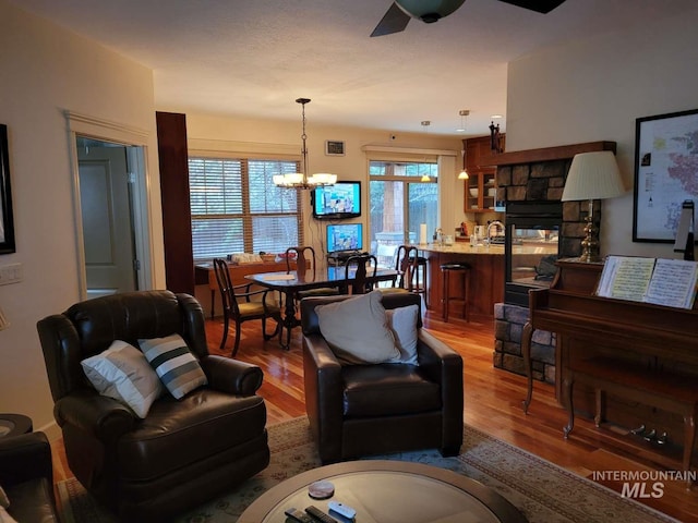 living room featuring hardwood / wood-style floors, ceiling fan with notable chandelier, and a fireplace