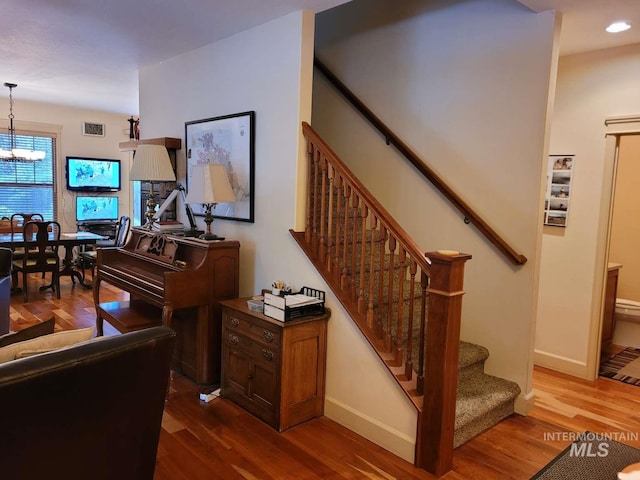 staircase with wood-type flooring and an inviting chandelier