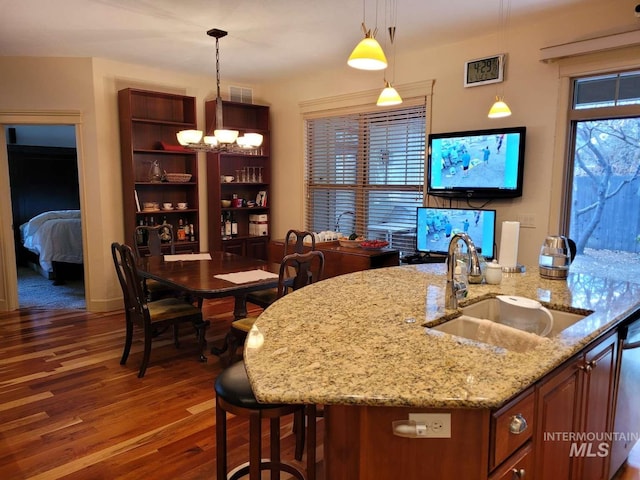 kitchen featuring dark wood-type flooring, sink, a chandelier, light stone counters, and pendant lighting