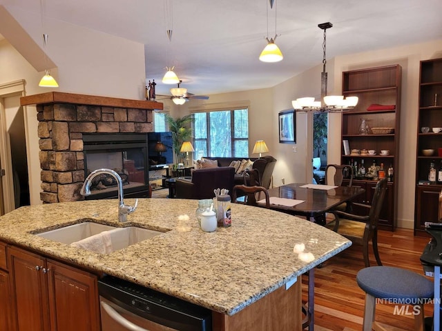 kitchen with hanging light fixtures, ceiling fan with notable chandelier, a kitchen island with sink, a fireplace, and dishwasher