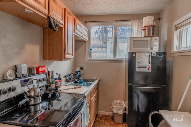 kitchen featuring sink, a textured ceiling, black fridge, and stainless steel range with electric stovetop