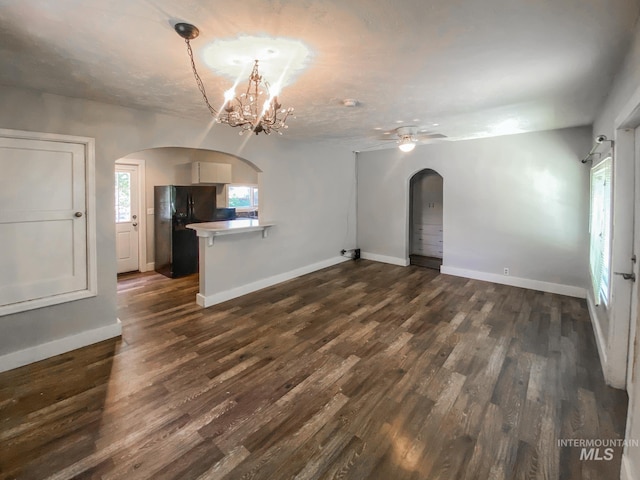 unfurnished living room featuring ceiling fan with notable chandelier and dark hardwood / wood-style floors