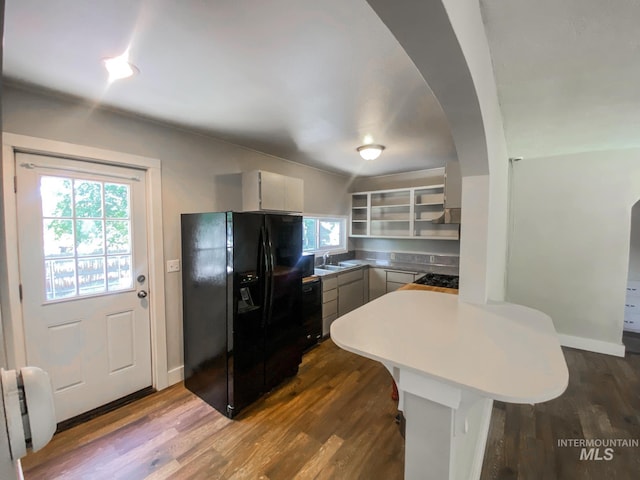 kitchen featuring kitchen peninsula, dark hardwood / wood-style flooring, sink, a breakfast bar, and black appliances