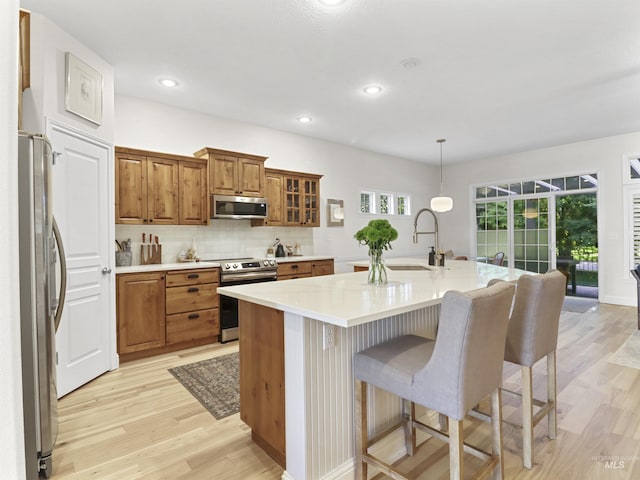 1262 N Forestdale Pl, Eagle, ID 83616 - kitchen with stainless steel appliances, brown cabinets, light wood finished floors, a kitchen breakfast bar, and an island with sink
