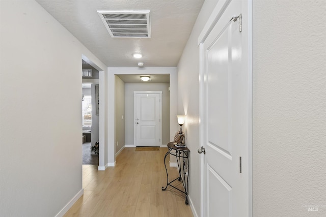 hall featuring light wood-type flooring, visible vents, and baseboards