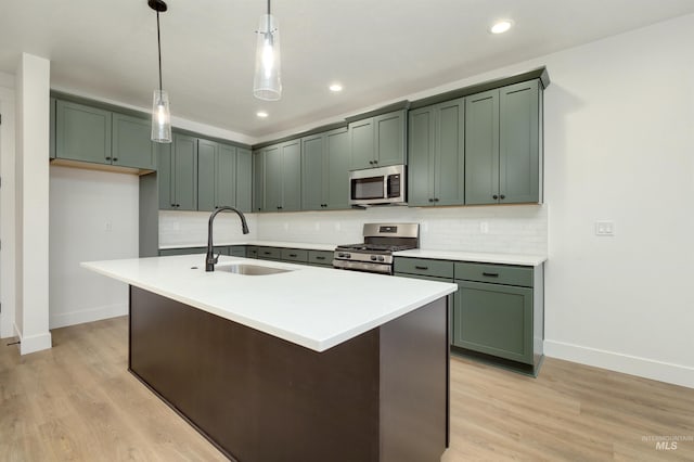 kitchen featuring a kitchen island with sink, sink, stainless steel appliances, and decorative light fixtures