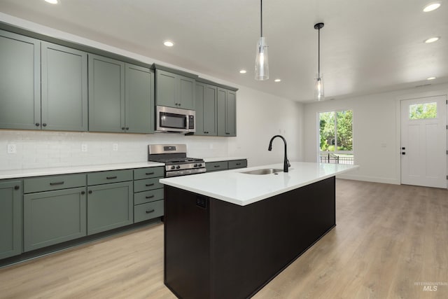 kitchen featuring appliances with stainless steel finishes, light wood-type flooring, sink, pendant lighting, and an island with sink