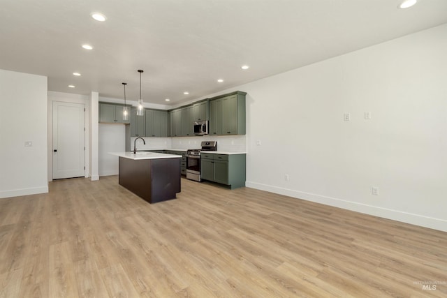 kitchen featuring decorative light fixtures, light hardwood / wood-style floors, stainless steel appliances, and an island with sink