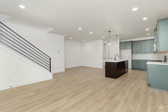 kitchen featuring backsplash, a kitchen island with sink, sink, pendant lighting, and light hardwood / wood-style floors