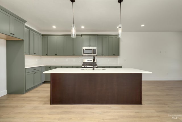 kitchen featuring a kitchen island with sink, sink, stainless steel appliances, and decorative light fixtures