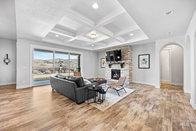 living room featuring beamed ceiling, a fireplace, light wood-style floors, arched walkways, and coffered ceiling