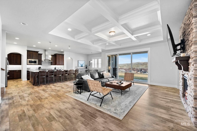 living area featuring beam ceiling, coffered ceiling, a fireplace, light wood finished floors, and baseboards