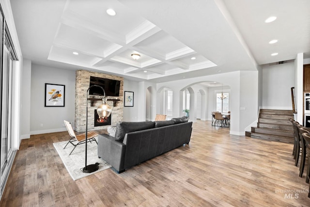 living area with light wood-type flooring, coffered ceiling, recessed lighting, arched walkways, and a fireplace