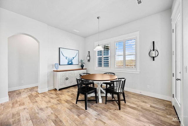 dining area with visible vents, light wood-style flooring, baseboards, and arched walkways