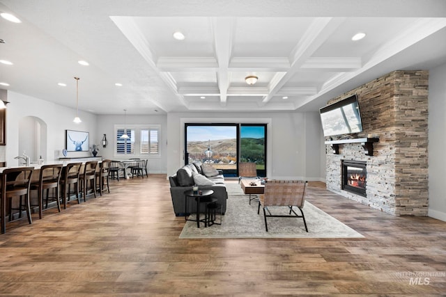 living area featuring wood finished floors, baseboards, coffered ceiling, a fireplace, and beamed ceiling