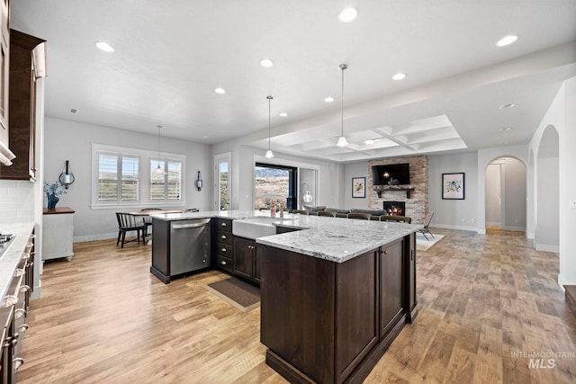 kitchen with light wood finished floors, a sink, a stone fireplace, dark brown cabinets, and dishwasher