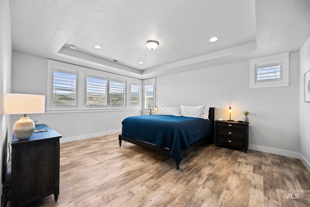 bedroom with visible vents, a raised ceiling, baseboards, and wood finished floors