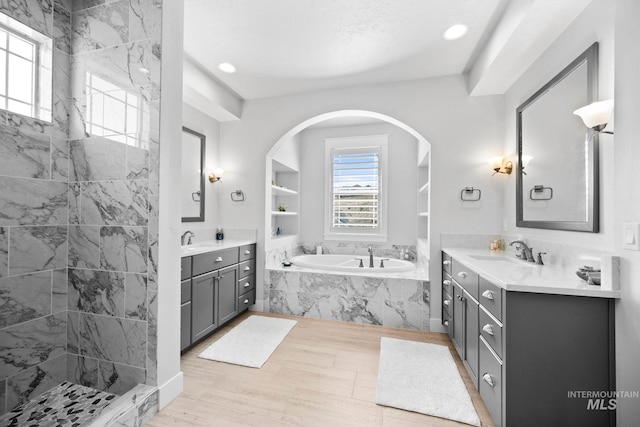 full bath featuring tiled shower, two vanities, a bath, and a sink