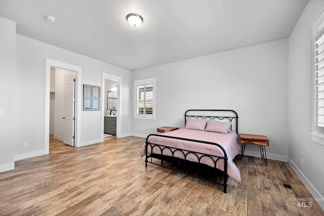 bedroom with light wood-style flooring, baseboards, visible vents, and connected bathroom