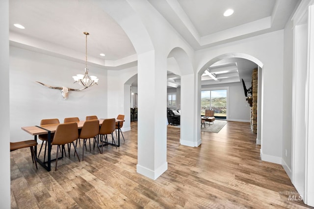 dining space with a notable chandelier, a raised ceiling, baseboards, and wood finished floors