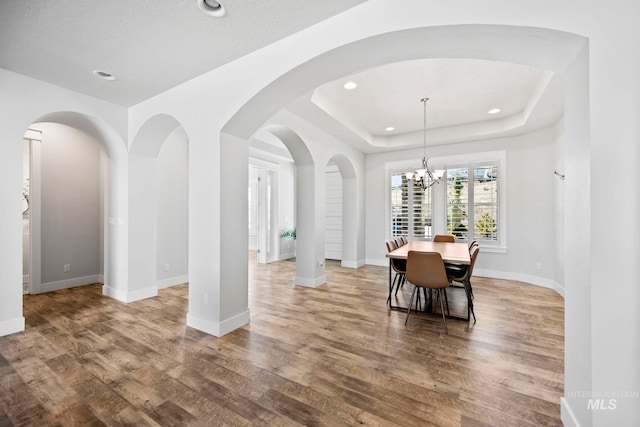 dining space with baseboards, a tray ceiling, recessed lighting, wood finished floors, and a notable chandelier