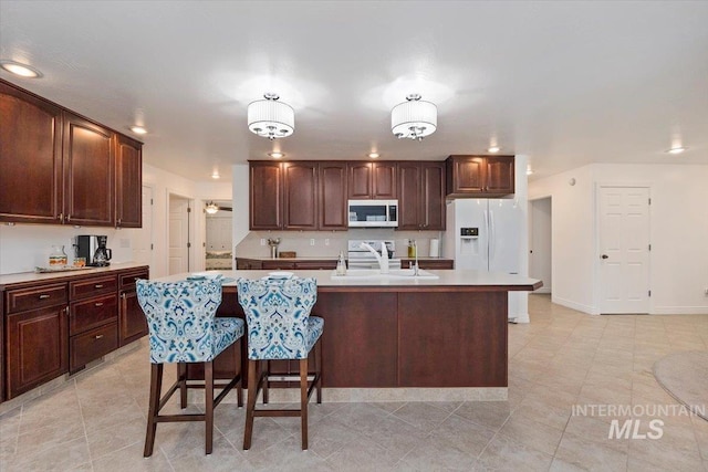 kitchen featuring a center island with sink, stainless steel microwave, light countertops, white fridge with ice dispenser, and a sink