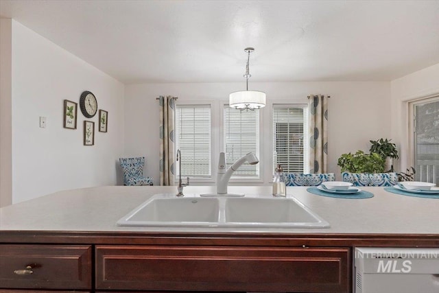 kitchen featuring dark brown cabinetry, dishwashing machine, decorative light fixtures, light countertops, and a sink