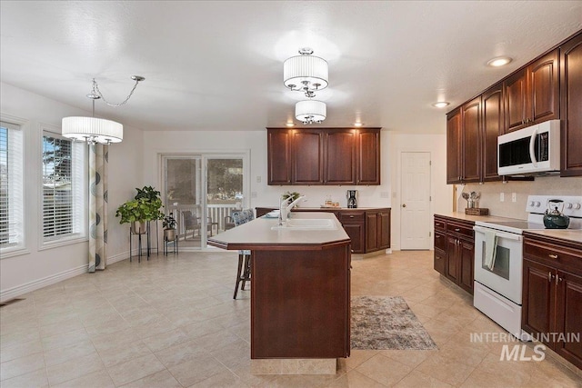 kitchen with white appliances, a center island with sink, light countertops, and a sink