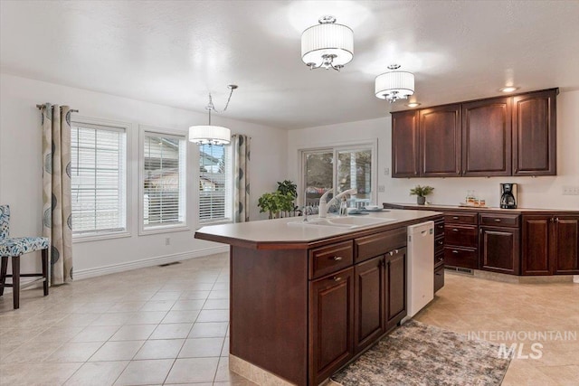 kitchen with white dishwasher, a sink, a healthy amount of sunlight, an island with sink, and pendant lighting