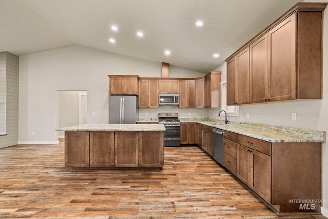 kitchen with stainless steel appliances, sink, a center island, vaulted ceiling, and light hardwood / wood-style floors