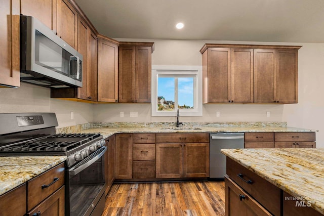 kitchen with hardwood / wood-style floors, sink, light stone counters, and stainless steel appliances