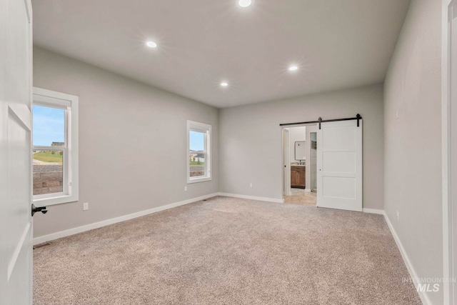 unfurnished bedroom with multiple windows, a barn door, and light colored carpet