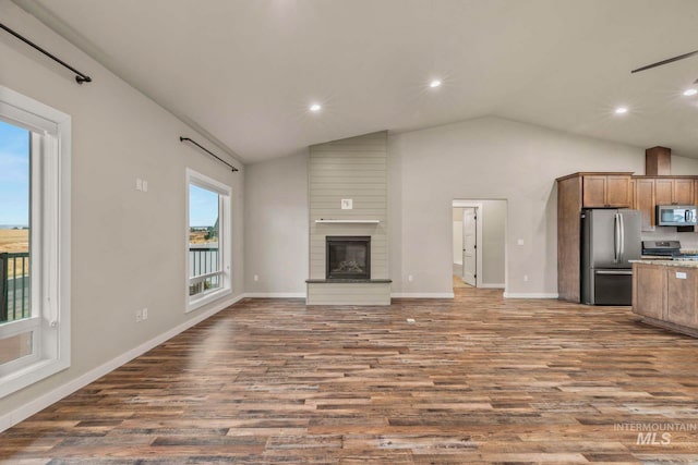 unfurnished living room featuring a healthy amount of sunlight, a large fireplace, and dark wood-type flooring