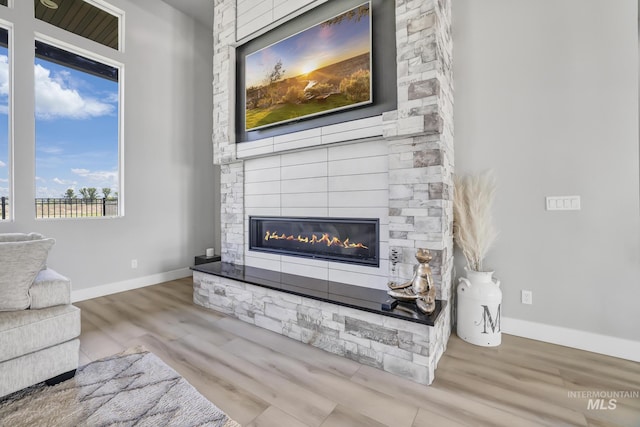 living room featuring a stone fireplace, wood finished floors, and baseboards