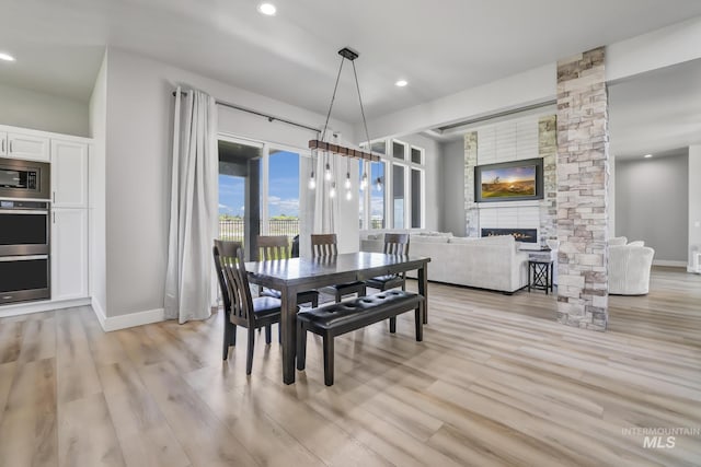 dining space featuring light wood-type flooring, recessed lighting, and a stone fireplace