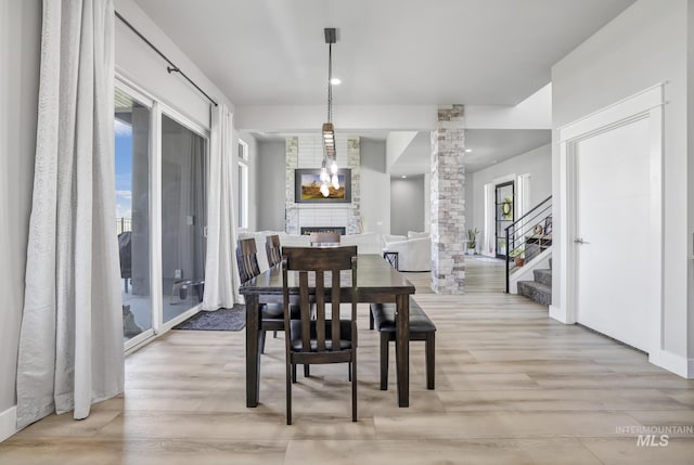 dining room with light wood-type flooring, a fireplace, decorative columns, and stairway