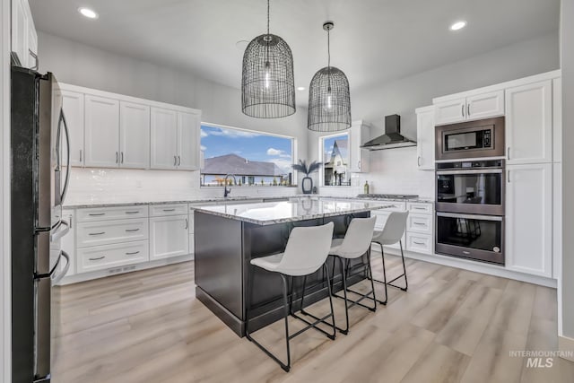 kitchen featuring wall chimney exhaust hood, appliances with stainless steel finishes, a center island, and white cabinets