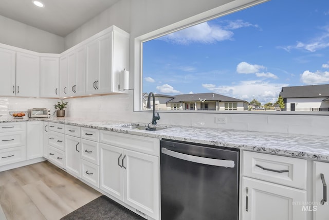 kitchen featuring light stone countertops, stainless steel dishwasher, light wood-style floors, white cabinetry, and a sink