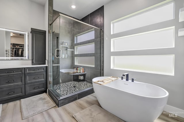 bathroom with a shower stall, a freestanding bath, and wood finished floors