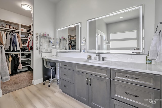 bathroom featuring a spacious closet, tasteful backsplash, wood finished floors, and vanity