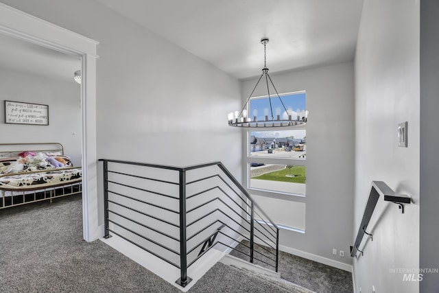 hall with baseboards, carpet flooring, an upstairs landing, and an inviting chandelier