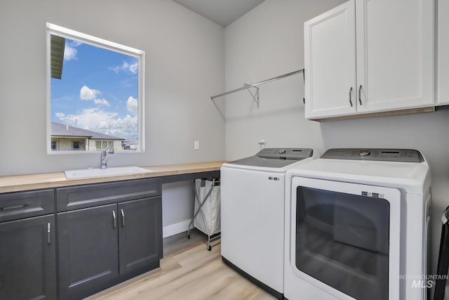 washroom with light wood-style flooring, cabinet space, a sink, and washer and clothes dryer