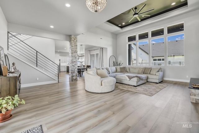 living room featuring stairs, baseboards, a raised ceiling, and light wood-style floors