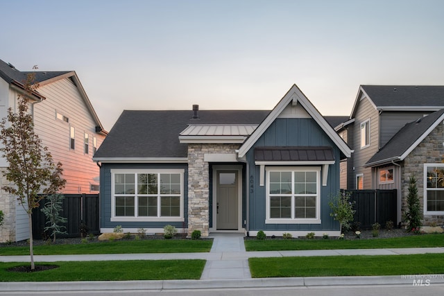 view of front facade featuring board and batten siding, metal roof, fence, and a lawn