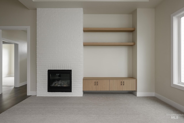 unfurnished living room featuring a brick fireplace, carpet flooring, and baseboards