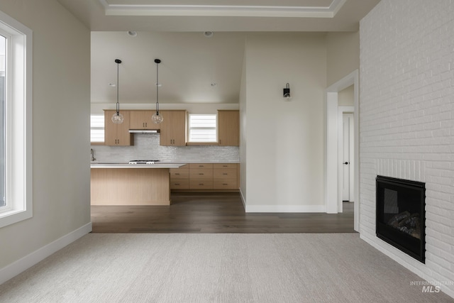 kitchen featuring open floor plan, light countertops, a brick fireplace, light brown cabinetry, and tasteful backsplash