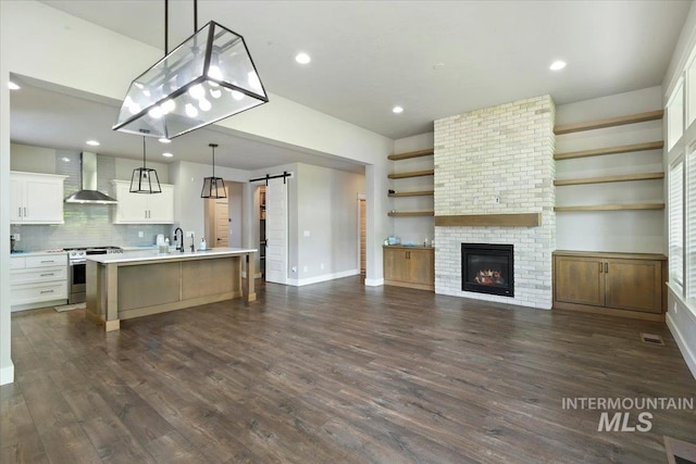 3303 S Island Fox Ave, Eagle, ID 83616 - kitchen with stainless steel range, a barn door, wall chimney range hood, light countertops, and a kitchen island with sink
